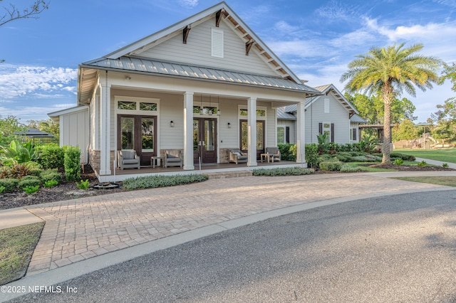 view of front of property featuring a standing seam roof, decorative driveway, french doors, covered porch, and metal roof