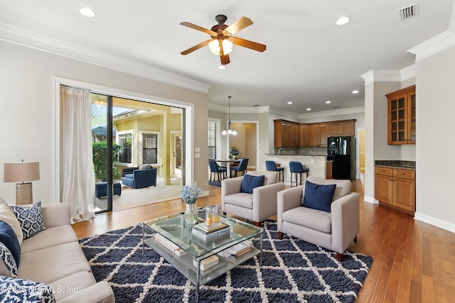 living area featuring a ceiling fan, wood finished floors, visible vents, recessed lighting, and crown molding