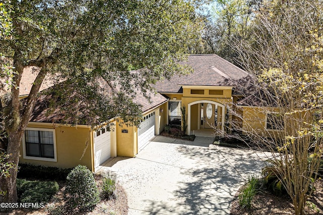 view of front of home with stucco siding, a garage, roof with shingles, and driveway