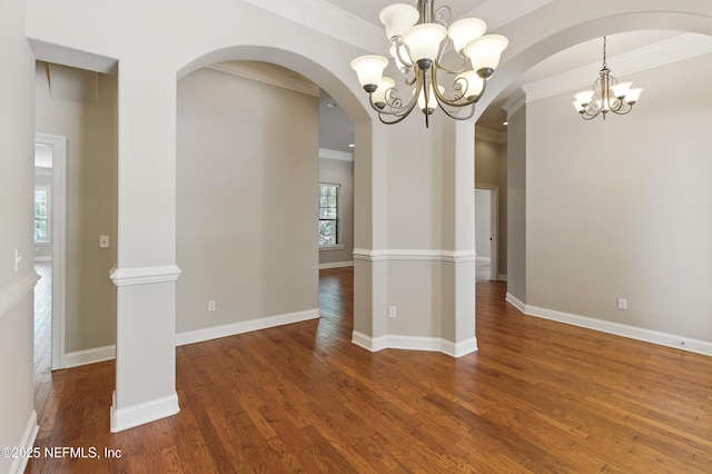 unfurnished dining area with ornamental molding, wood finished floors, arched walkways, an inviting chandelier, and baseboards