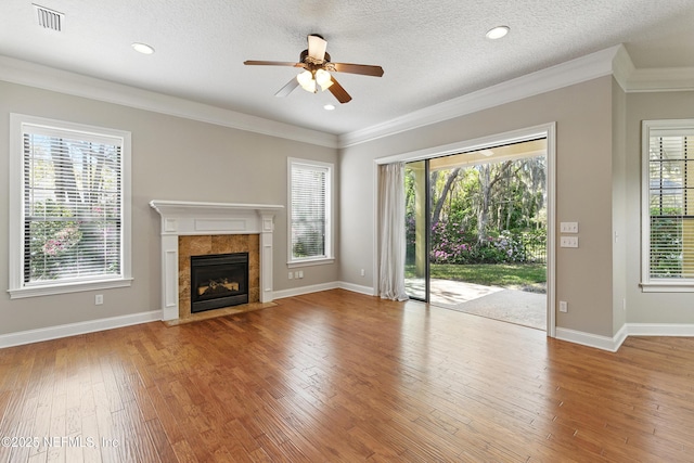 unfurnished living room featuring a ceiling fan, visible vents, baseboards, hardwood / wood-style flooring, and crown molding