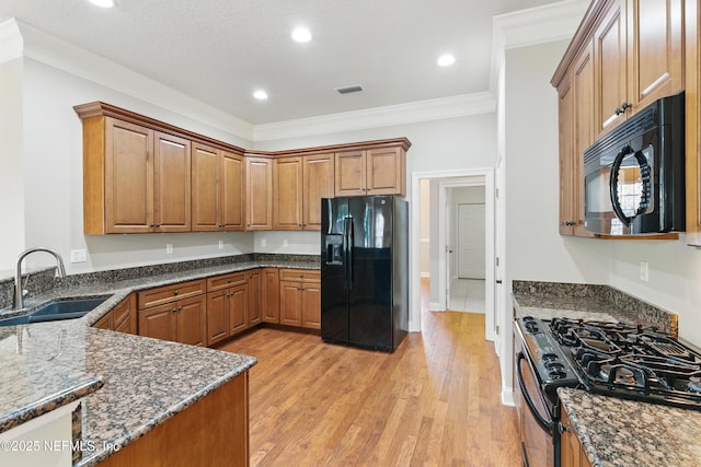 kitchen with a sink, light wood-style floors, black appliances, and dark stone countertops