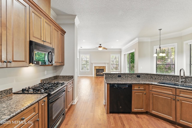 kitchen with a tile fireplace, a sink, black appliances, light wood-style floors, and ceiling fan with notable chandelier