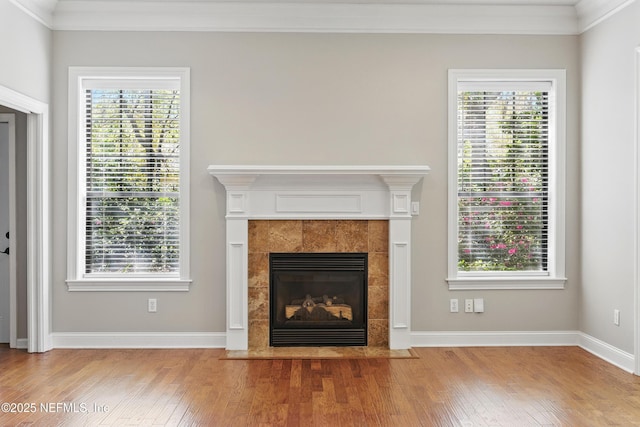 unfurnished living room featuring a tiled fireplace, crown molding, baseboards, and hardwood / wood-style flooring