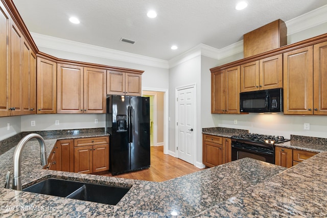 kitchen featuring visible vents, black appliances, a sink, brown cabinetry, and crown molding