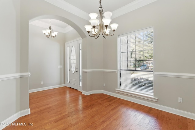 foyer featuring wood finished floors, baseboards, an inviting chandelier, arched walkways, and ornamental molding