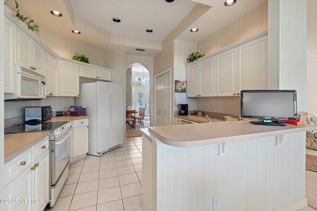 523 Lakeway Dr, Saint Augustine, FL 32080 - kitchen featuring white appliances, light tile patterned floors, wallpapered walls, arched walkways, and white cabinets