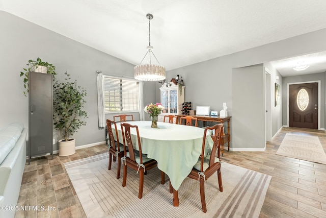 dining space featuring light wood finished floors, a notable chandelier, baseboards, and vaulted ceiling