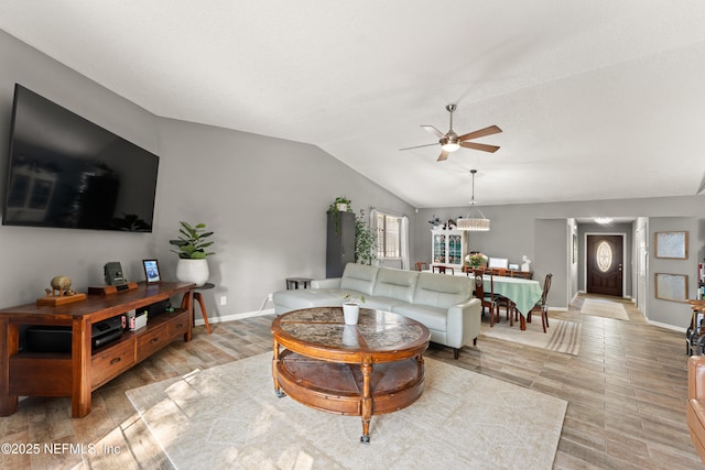 living area with ceiling fan with notable chandelier, baseboards, light wood-style flooring, and lofted ceiling