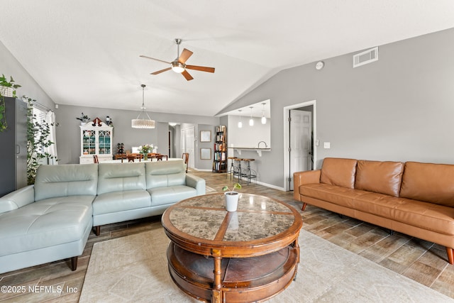 living area with wood finish floors, visible vents, baseboards, ceiling fan, and vaulted ceiling