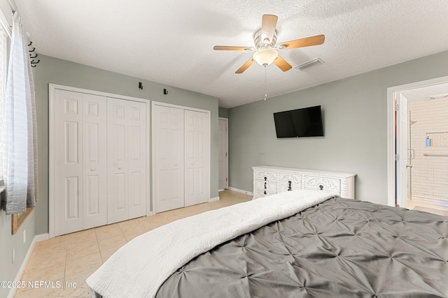 bedroom with visible vents, light tile patterned flooring, multiple closets, a textured ceiling, and connected bathroom