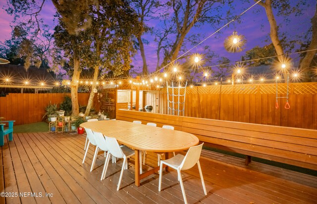 deck at dusk featuring outdoor dining space and a fenced backyard