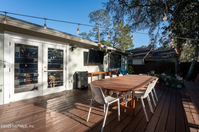 wooden terrace with french doors, outdoor dining space, and fence