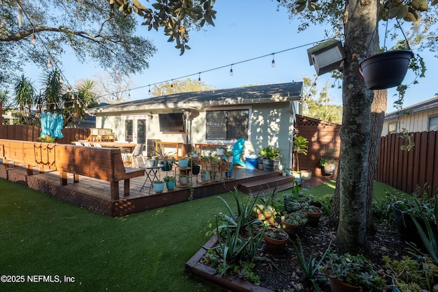 rear view of property with stucco siding, fence, a lawn, and a wooden deck