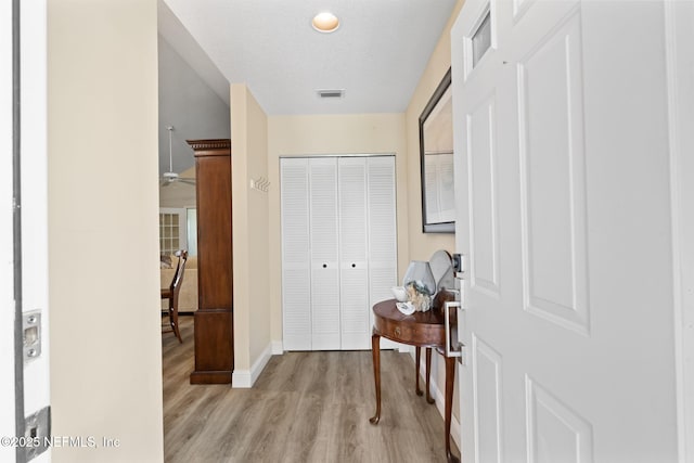 corridor with baseboards, visible vents, light wood finished floors, and a textured ceiling