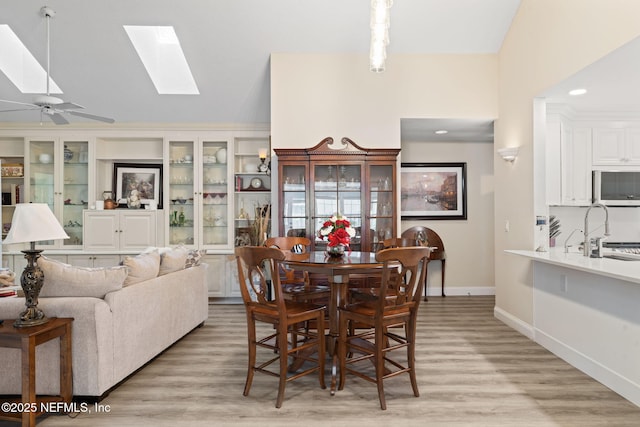 dining room with a ceiling fan, lofted ceiling with skylight, baseboards, and light wood-type flooring