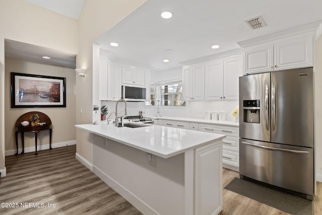 kitchen featuring light wood finished floors, a peninsula, white cabinets, stainless steel appliances, and a sink