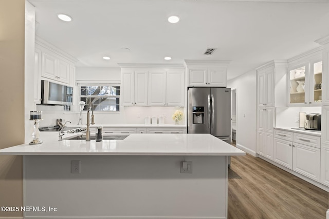 kitchen featuring visible vents, a sink, wood finished floors, white cabinetry, and appliances with stainless steel finishes