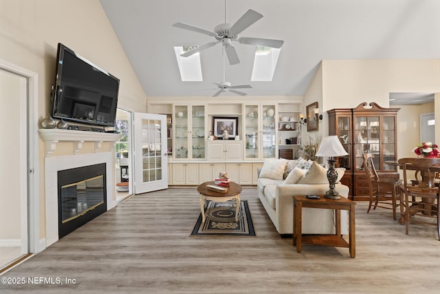 living room with ceiling fan, built in features, a skylight, wood finished floors, and a glass covered fireplace