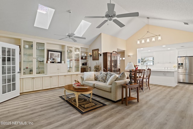 living area featuring visible vents, high vaulted ceiling, a skylight, a textured ceiling, and light wood-type flooring