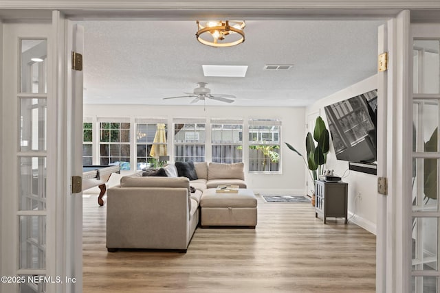 living area with ceiling fan, visible vents, light wood-type flooring, and a textured ceiling