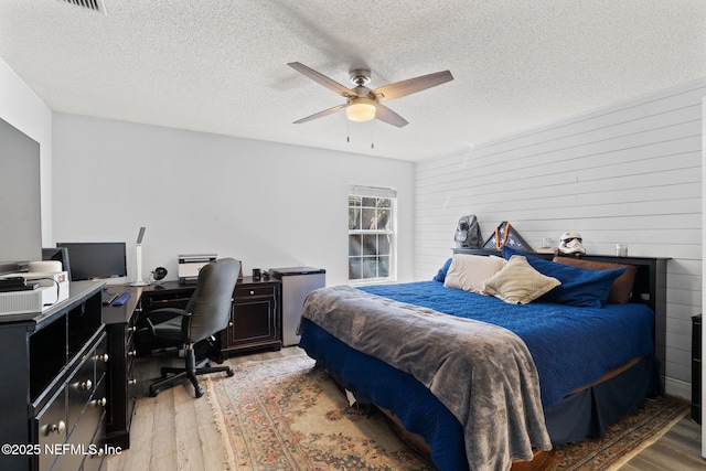 bedroom featuring light wood-type flooring, a textured ceiling, wood walls, and a ceiling fan