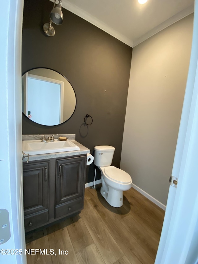 half bath featuring toilet, wood finished floors, crown molding, baseboards, and vanity