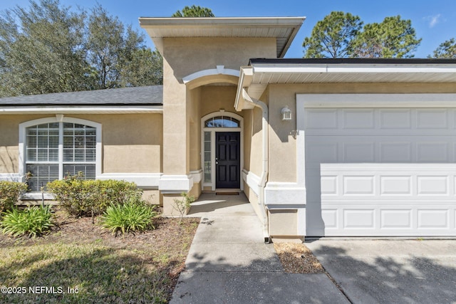 view of exterior entry featuring an attached garage, driveway, and stucco siding