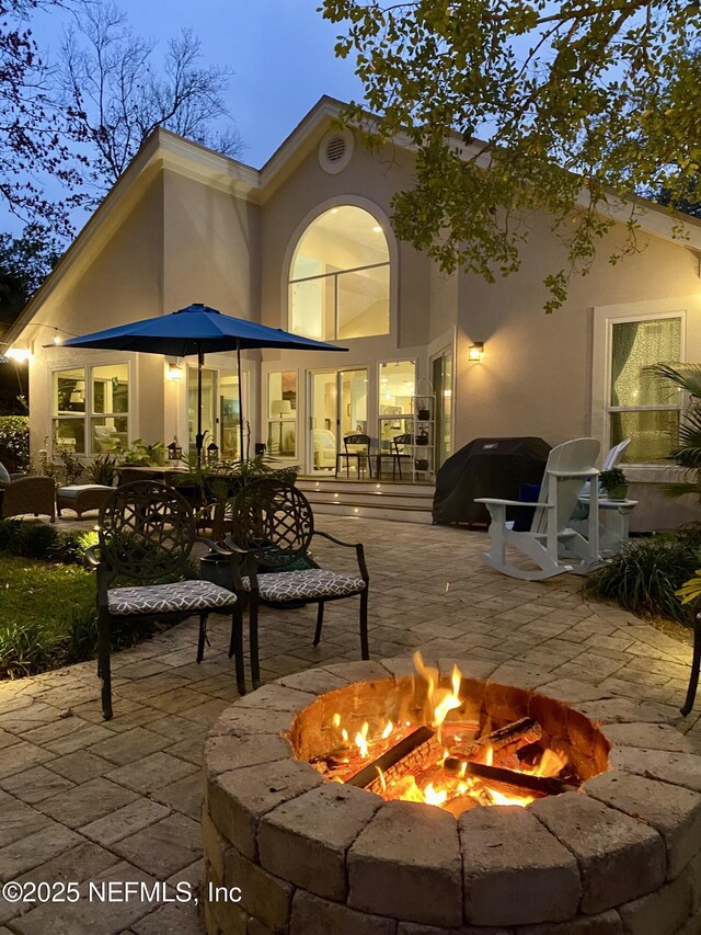 rear view of house with a patio, a fire pit, and stucco siding