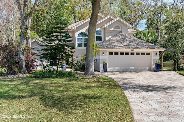 traditional home with stucco siding, a front lawn, decorative driveway, roof with shingles, and an attached garage