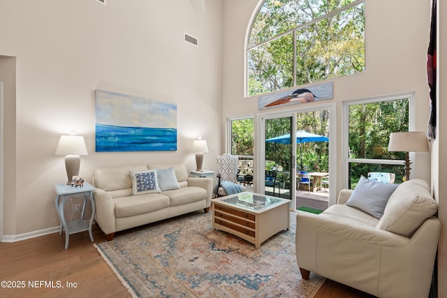 living area featuring visible vents, baseboards, a towering ceiling, and wood finished floors