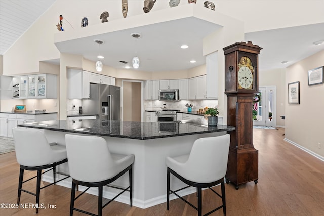 kitchen with backsplash, white cabinetry, appliances with stainless steel finishes, a peninsula, and light wood finished floors