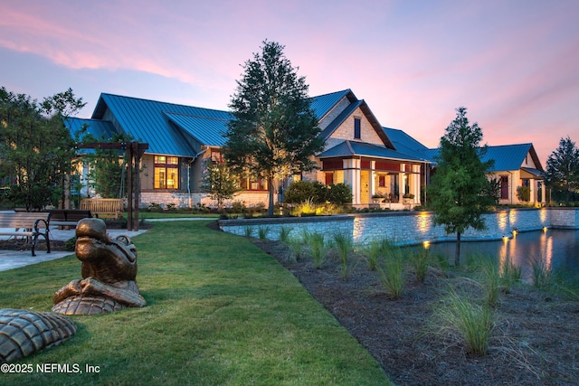 back of house at dusk featuring metal roof, a lawn, and a standing seam roof