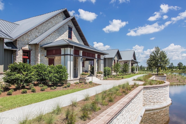 exterior space with stone siding, metal roof, a water view, and a standing seam roof