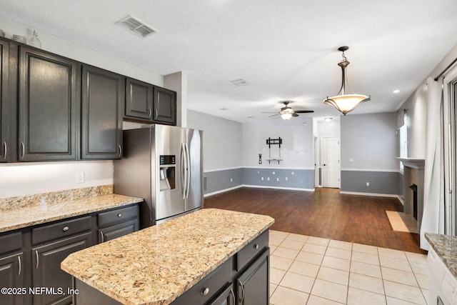 1601 Majestic View Ln, Fleming Island, FL 32003 - kitchen featuring stainless steel fridge with ice dispenser, a ceiling fan, a fireplace with flush hearth, light tile patterned flooring, and a center island