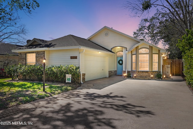 ranch-style home featuring fence, roof with shingles, driveway, stone siding, and an attached garage