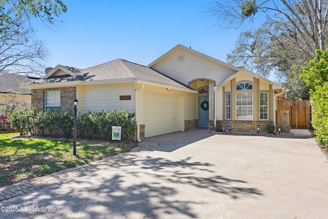 view of front of house with stone siding, fence, roof with shingles, concrete driveway, and a garage