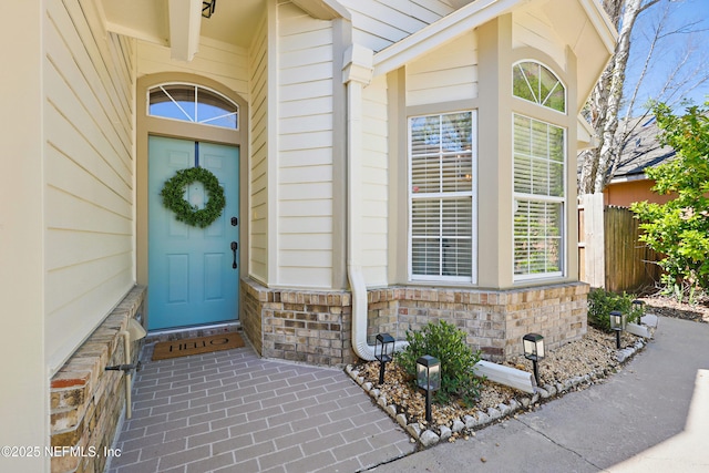 doorway to property featuring brick siding and fence