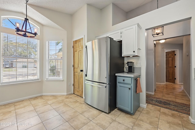 kitchen with decorative light fixtures, light tile patterned floors, freestanding refrigerator, an inviting chandelier, and white cabinets