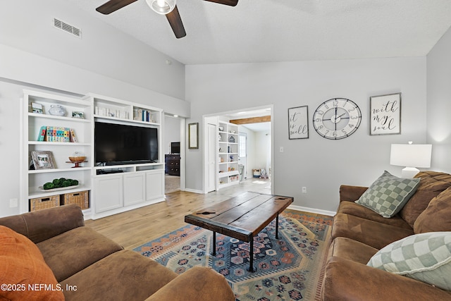 living room featuring light wood-type flooring, visible vents, a ceiling fan, baseboards, and lofted ceiling