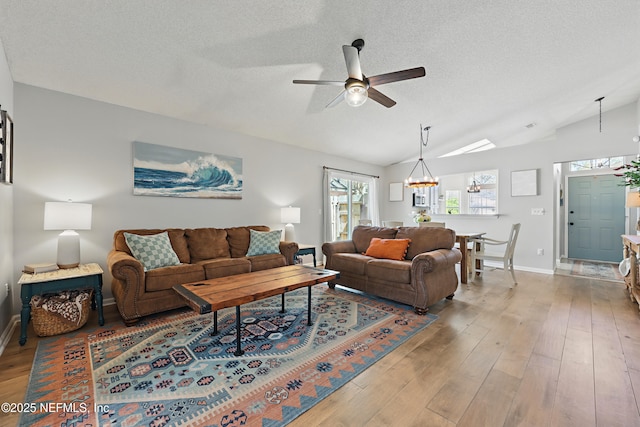 living area with a textured ceiling, ceiling fan with notable chandelier, light wood-style floors, and vaulted ceiling