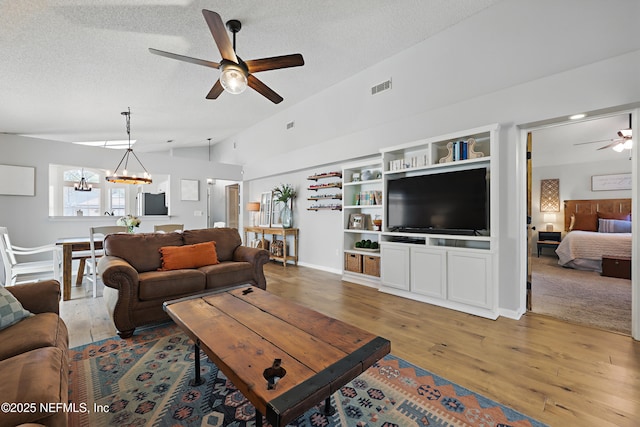 living room featuring light wood-type flooring, visible vents, ceiling fan with notable chandelier, a textured ceiling, and lofted ceiling