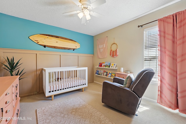 bedroom with a crib, a wainscoted wall, carpet floors, and a textured ceiling