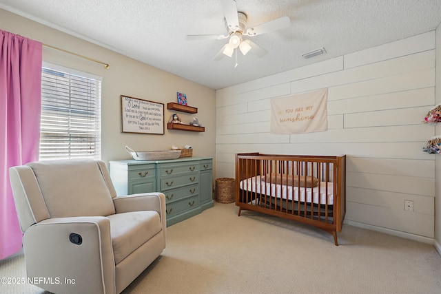 bedroom with a crib, a textured ceiling, light carpet, and ceiling fan