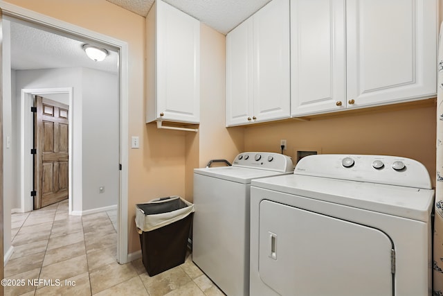 washroom with washer and dryer, a textured ceiling, cabinet space, light tile patterned flooring, and baseboards