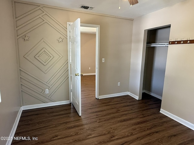 unfurnished bedroom with dark wood-style floors, visible vents, baseboards, and a closet