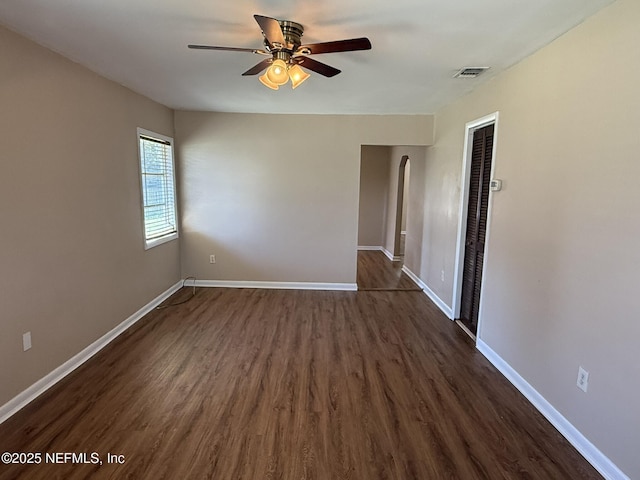 unfurnished room with arched walkways, ceiling fan, baseboards, and dark wood-style flooring