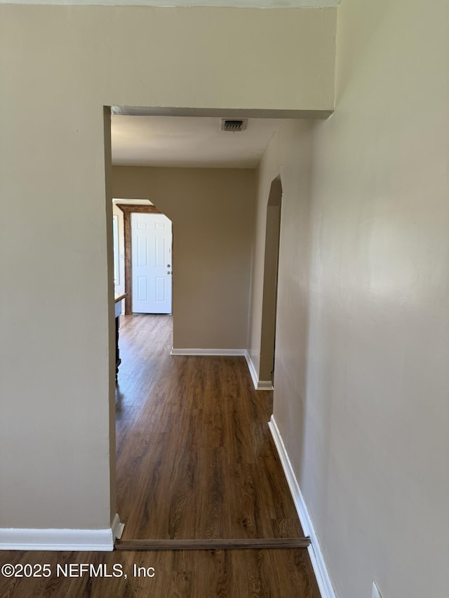 hallway with arched walkways, visible vents, baseboards, and wood finished floors