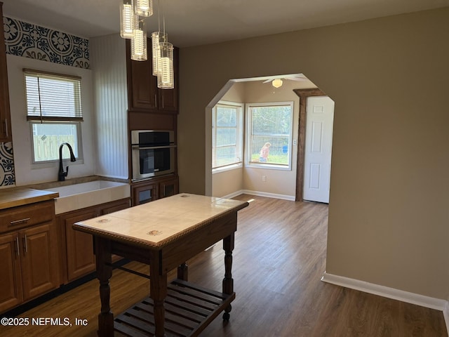 kitchen featuring baseboards, arched walkways, dark wood-style flooring, a sink, and stainless steel oven