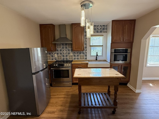 kitchen featuring tasteful backsplash, wood finished floors, stainless steel appliances, wall chimney exhaust hood, and a sink